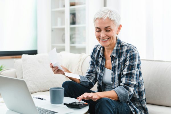 Happy mature Caucasian businesswoman having start-up plan, calculating funds a home with laptop.